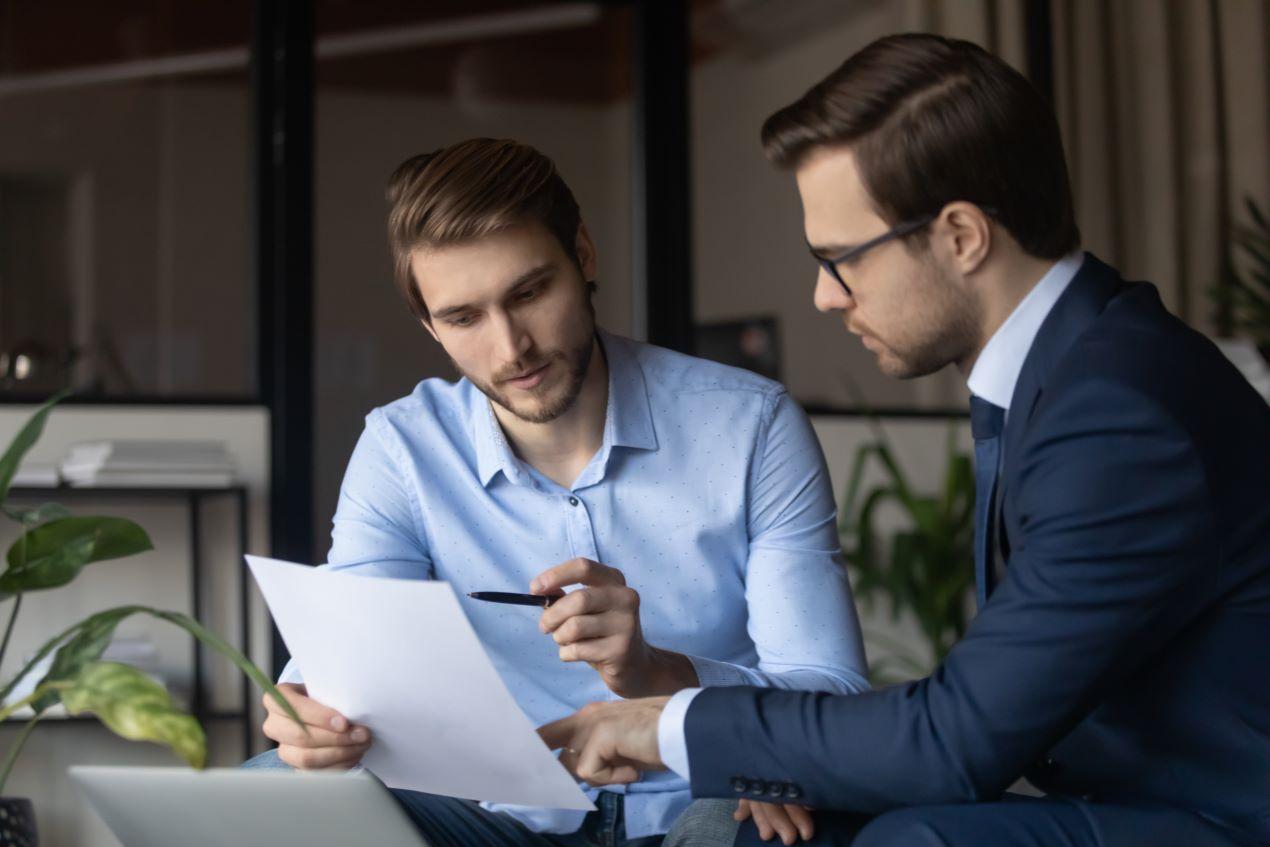 Zwei Geschäftsleute bei der Analyse eines Dokuments, symbolisch für Teamarbeit und Schulungen im Risiko-Management, inklusive regelmäßiger Sanktionsliste prüfen.