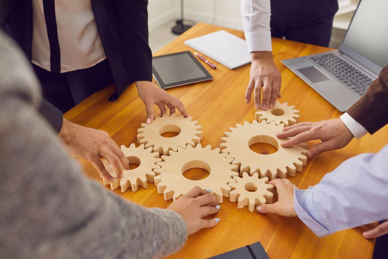 Teammitglieder arbeiten gemeinsam mit Holz-Zahnrädern an einem Tisch, symbolisieren die Integration und Zusammenarbeit bei der Implementierung von Keycloak.