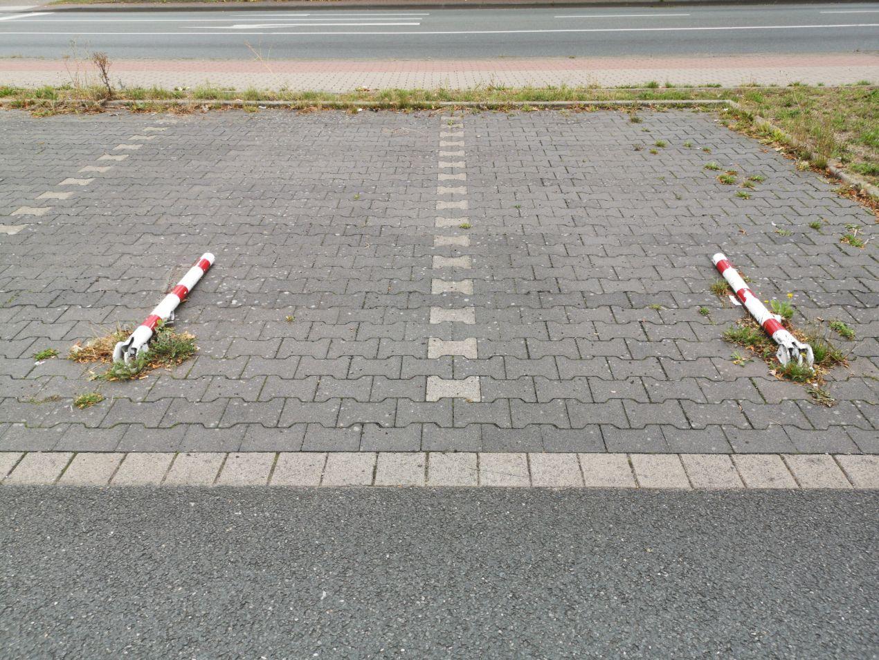 Zwei rot-weiße, heruntergeklappte Absperrpfosten auf einem Parkplatz zur temporären Freigabe der Stellflächen.