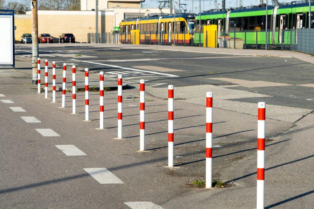 Weiße und rote Absperrpfosten entlang eines Fahrradwegs zur Abgrenzung vom Straßenverkehr in einer urbanen Umgebung.