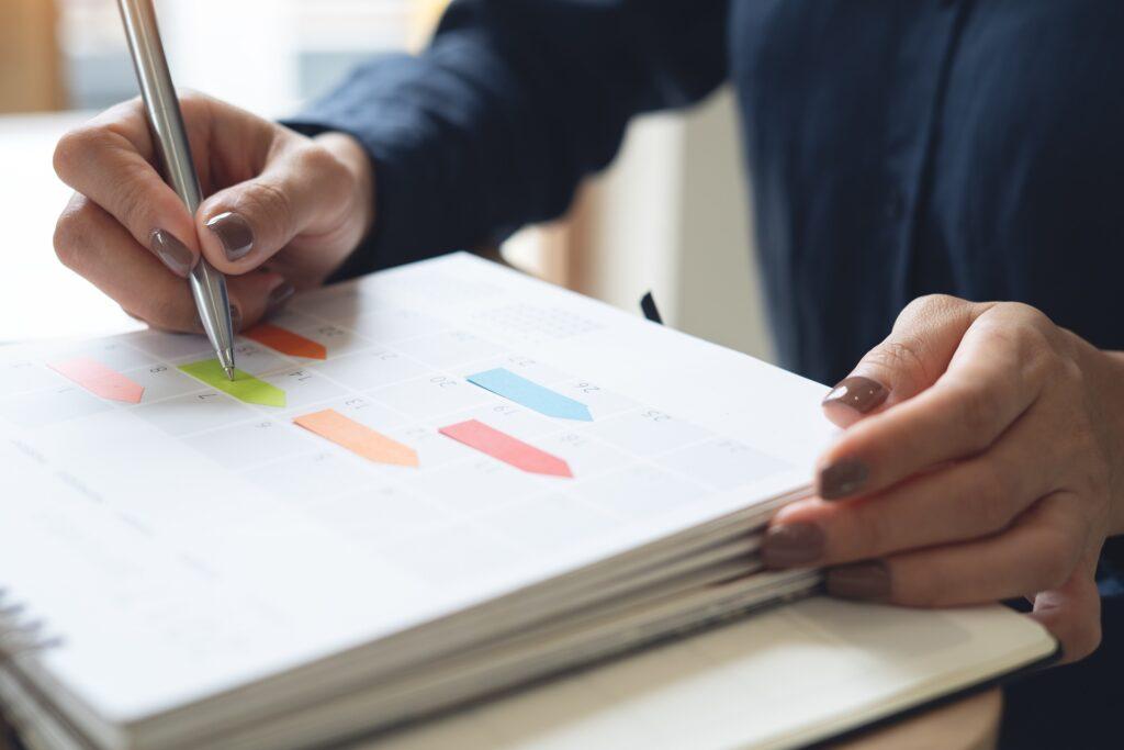 Person trägt Termine und Aufgaben in Papierkalender ein | Stehtisch